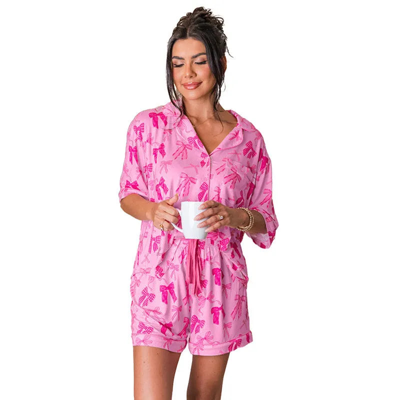 Pink women's pyjama set with bow print, featuring a top and trousers made from lightweight polyester fabric.
