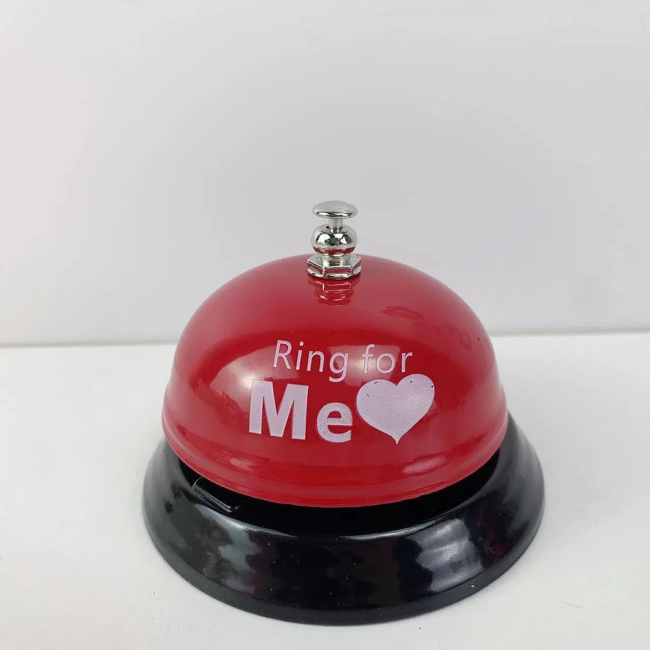 Iron call bell on a desk, shown in one of twelve available colours including red, blue, green, and pink.