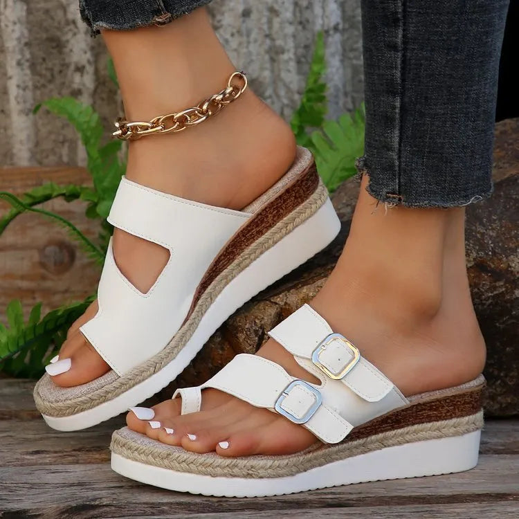 White wedge sandals with woven patent leather upper and open toe design on wooden surface