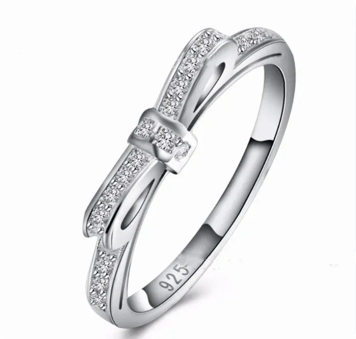 Silver bow-shaped ring with zircon crystals on a finger, showing detailed bow motif design