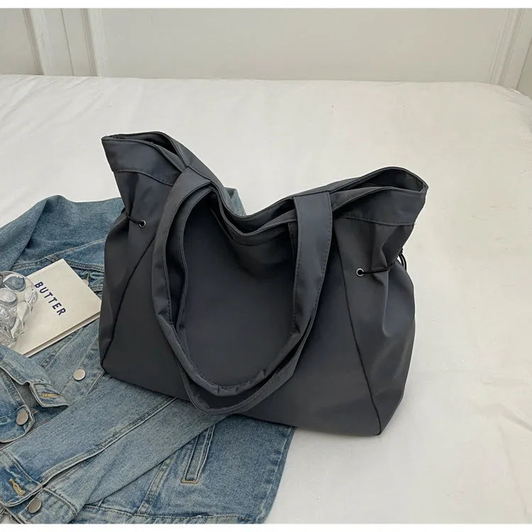 Soft Oxford cloth folding commuter tote bag shown in one of five colours: black, brown, dark grey, light grey or purple.