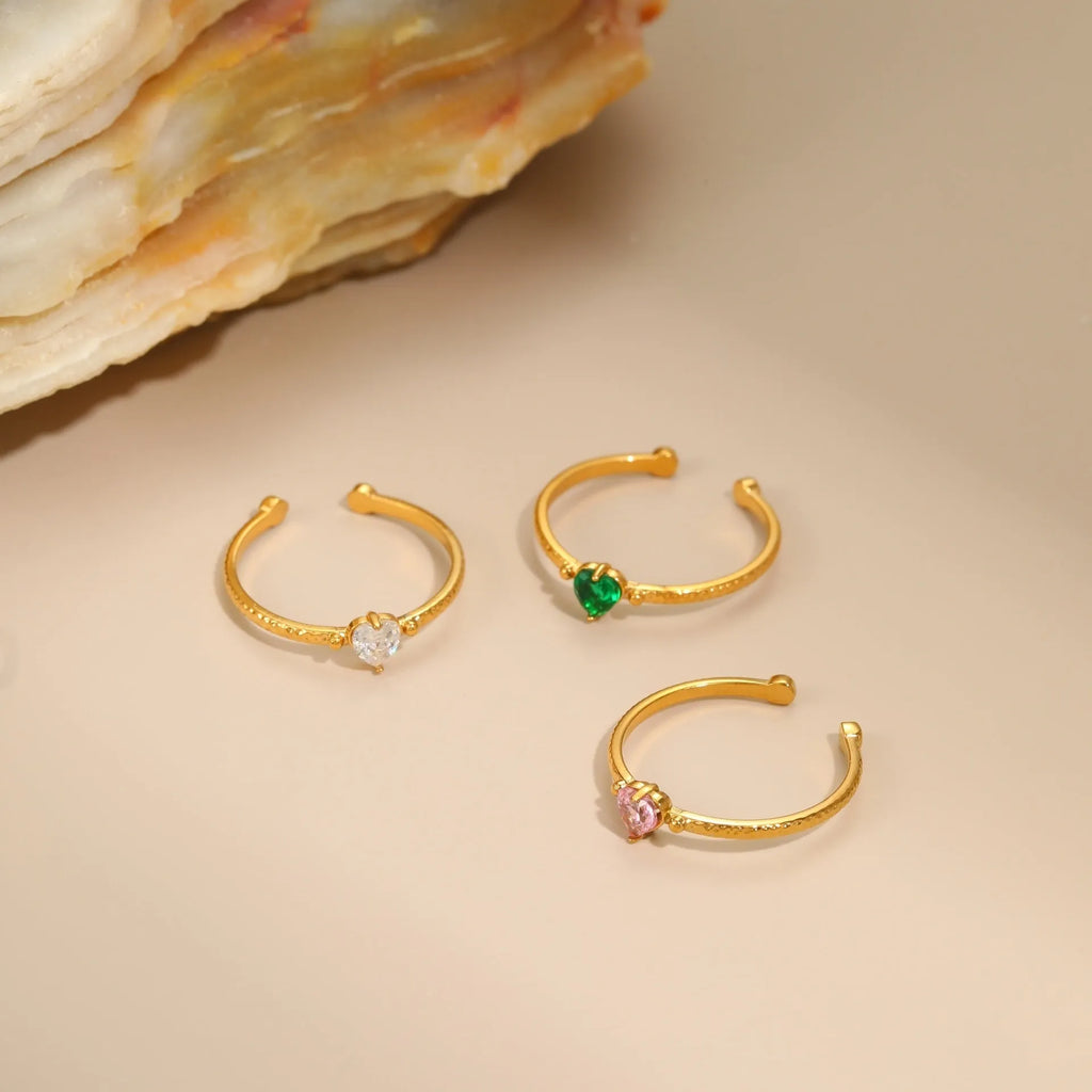 Open-ended stainless steel ring with a geometric heart shape inlaid with green zirconium on a plain background.