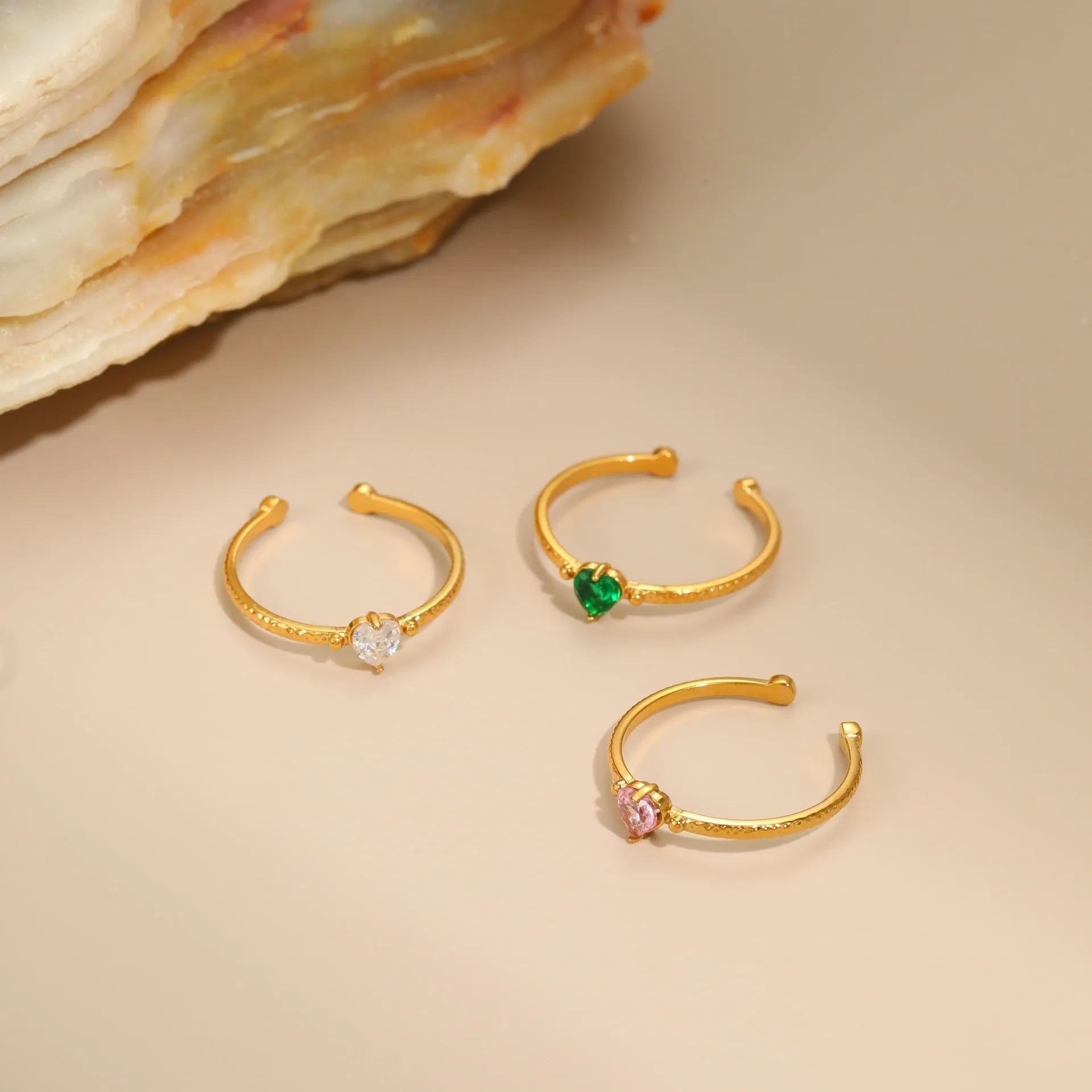 Open-ended stainless steel ring with a geometric heart shape inlaid with green zirconium on a plain background.