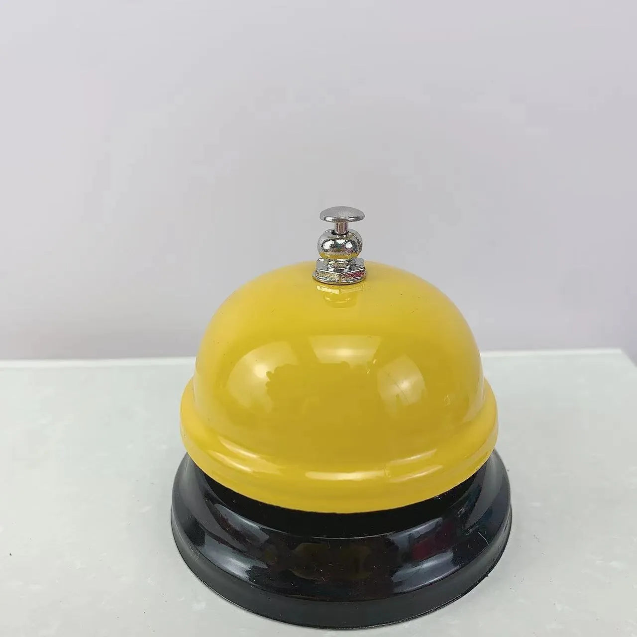 Iron call bell on a desk, shown in one of twelve available colours including red, blue, green, and pink.
