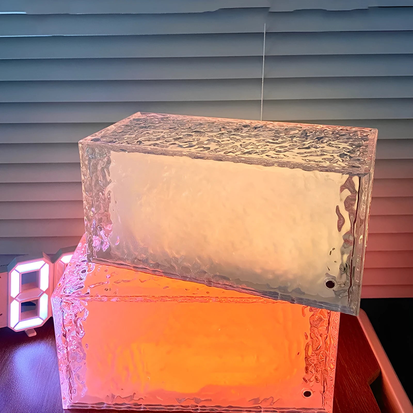 Clear acrylic ice cube shaped night lamp with coloured LED light on a table.