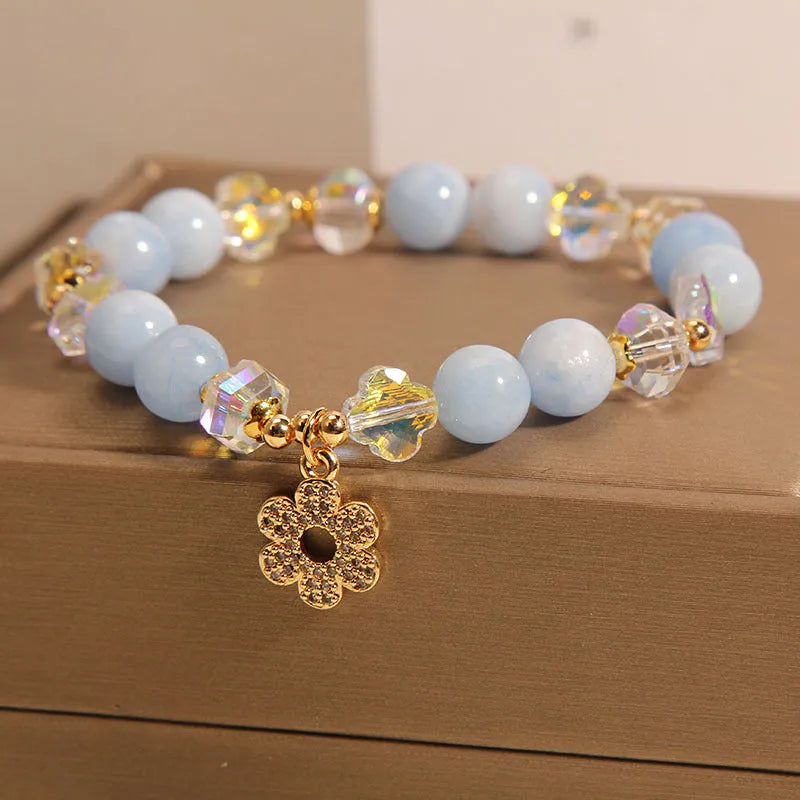 Women's aquamarine crystal bracelet with a four-leaf clover charm and pearl details on a white background