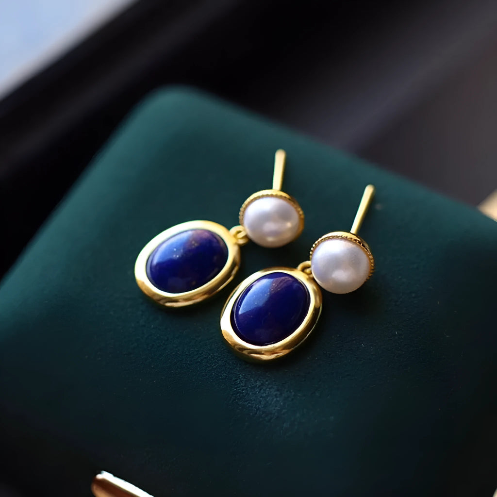 A pair of simple sterling silver stud earrings with blue lapis lazuli pearls and auspicious pattern details.