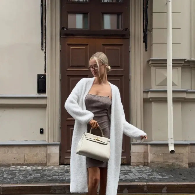 A woman wearing a long white knitted cardigan jacket with long sleeves and a loose fit.
