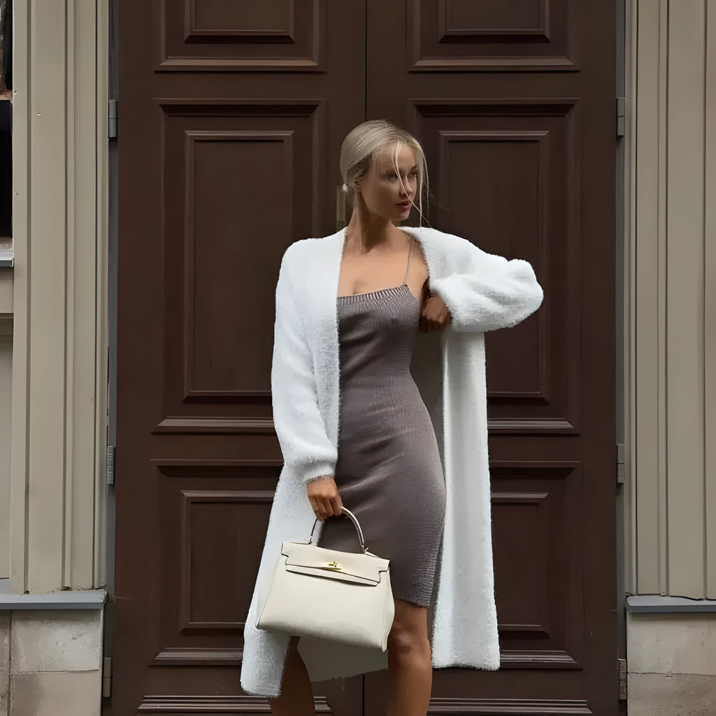 A woman wearing a long white knitted cardigan jacket with long sleeves and a loose fit.