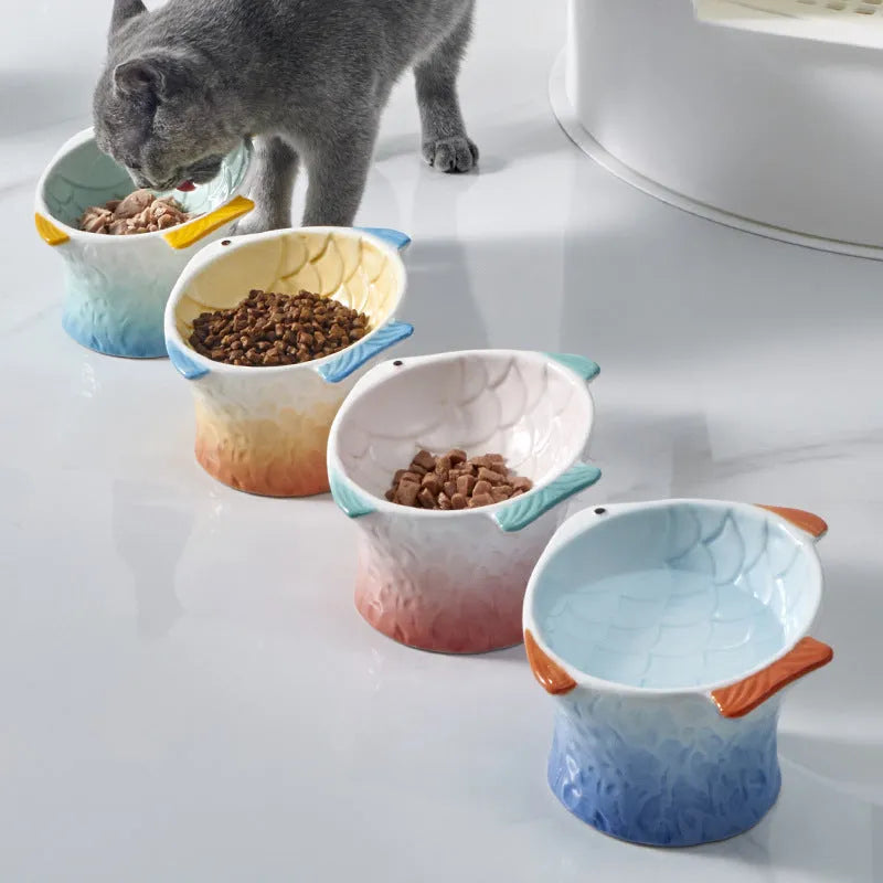 Set of four coloured fish-shaped ceramic cat bowls with a tilted, elevated design on a table.