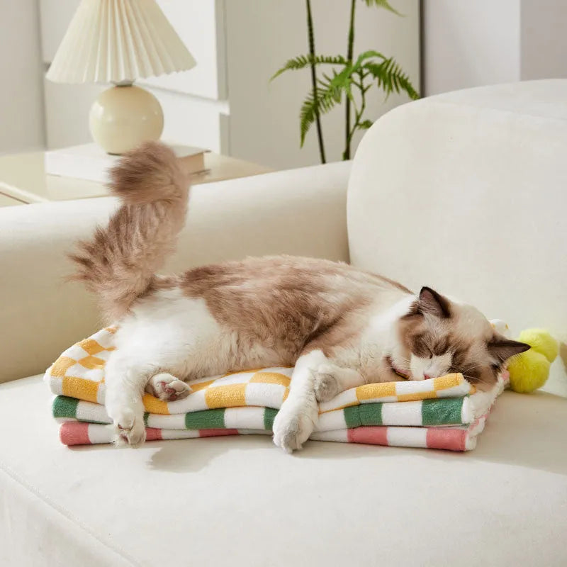 Green plaid patterned soft fleece pet blanket on a sofa, showing fur ball decoration.