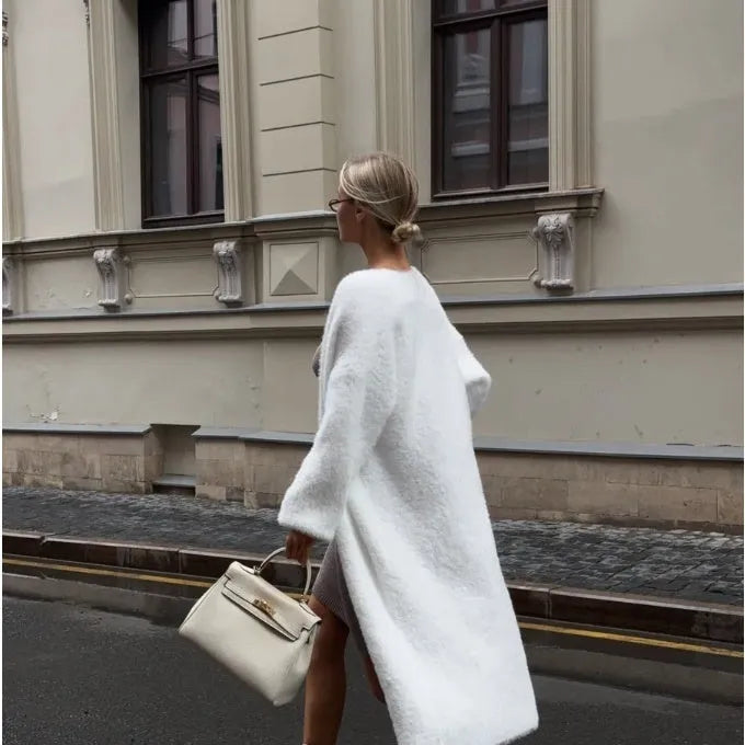 A woman wearing a long white knitted cardigan jacket with long sleeves and a loose fit.