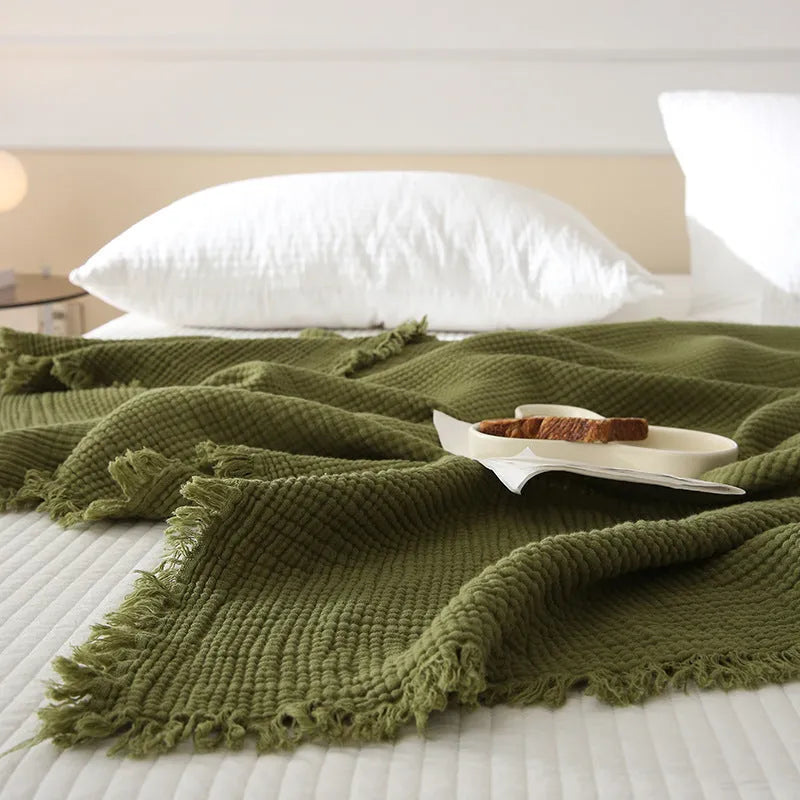 Four-layer cotton gauze blanket with tassel trim in avocado green colour laid flat.