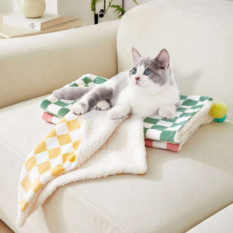 Green plaid patterned soft fleece pet blanket on a sofa, showing fur ball decoration.
