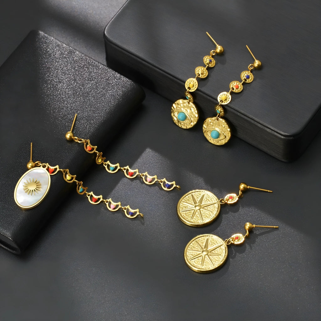 A pair of stainless steel geometric earrings showing star, eye, and shell sun designs.