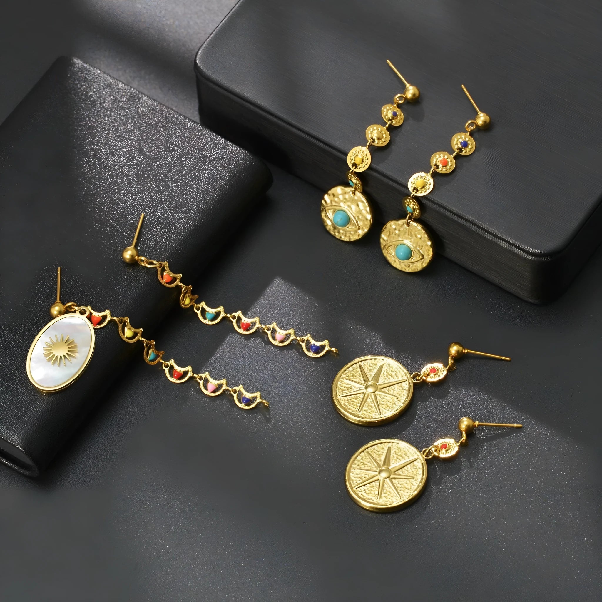 A pair of stainless steel geometric earrings showing star, eye, and shell sun designs.