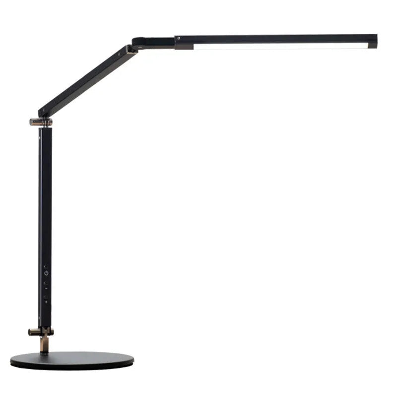 A black foldable LED desk lamp with a metal clip attached to a wooden desk edge, remote control nearby.