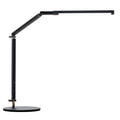 A black foldable LED desk lamp with a metal clip attached to a wooden desk edge, remote control nearby.