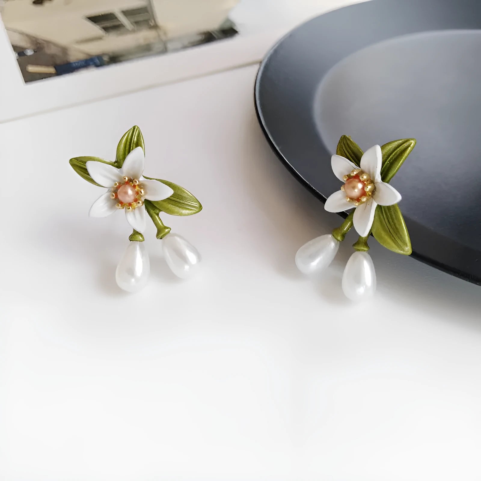 Close-up of women's camellia flower ear clip earrings with sterling silver needle accents on a contrasting background.