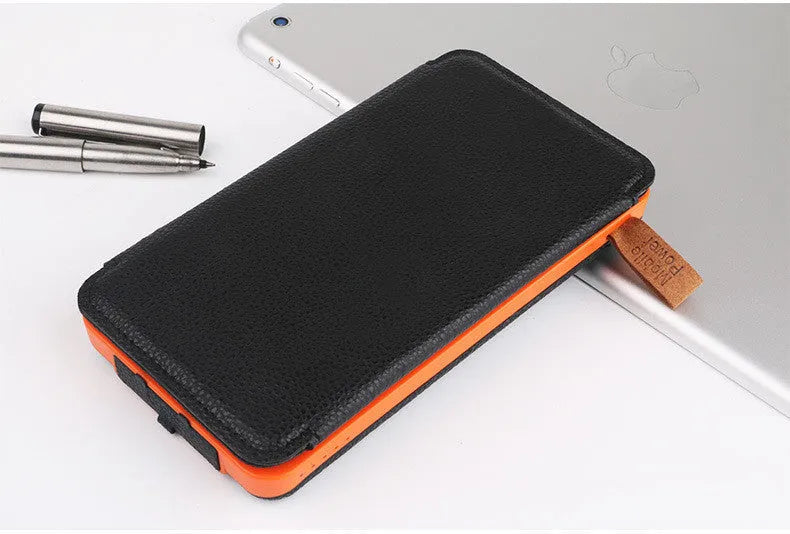 Black solar power bank with a solar panel, LED light, and soft leather exterior, shown outdoors.