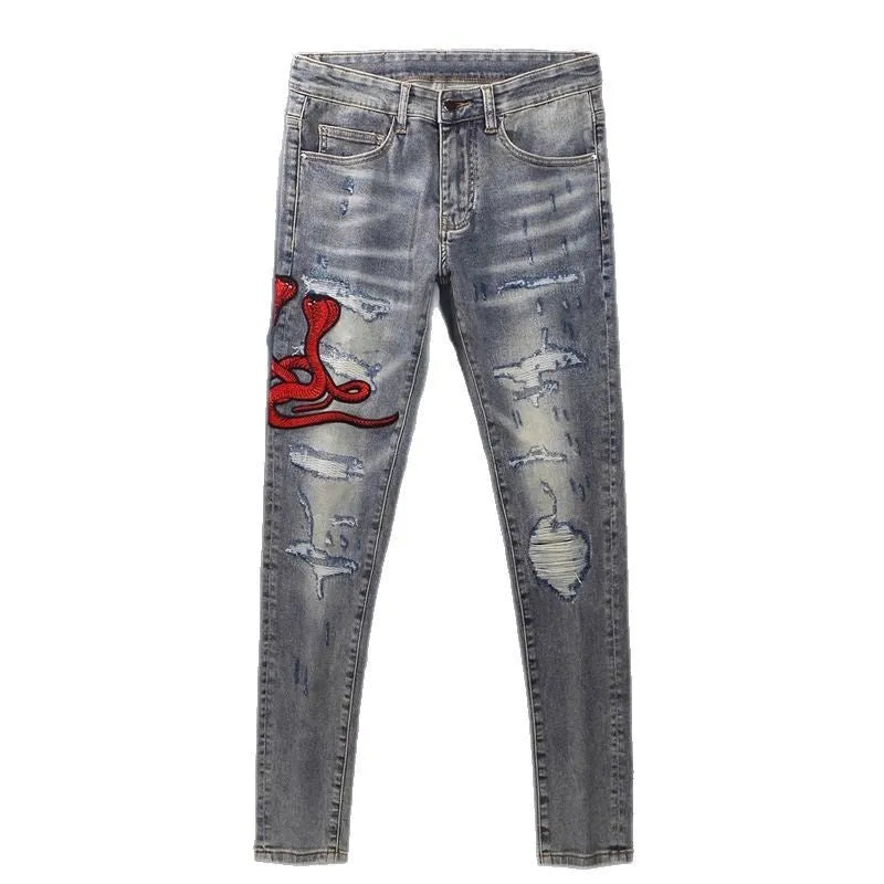Slim fit blue jeans with distressed hole patches and embroidery on the legs, showing a washed-out colour.