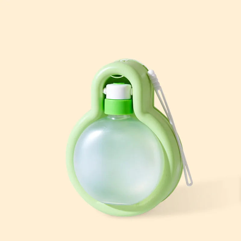 Green portable dog travel cup with pull-out bowl and handle, shown next to a backpack.
