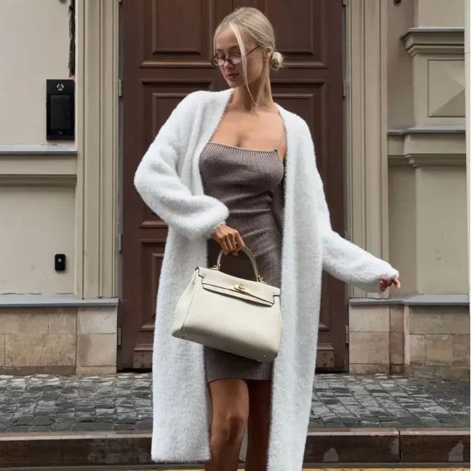 A woman wearing a long white knitted cardigan jacket with long sleeves and a loose fit.