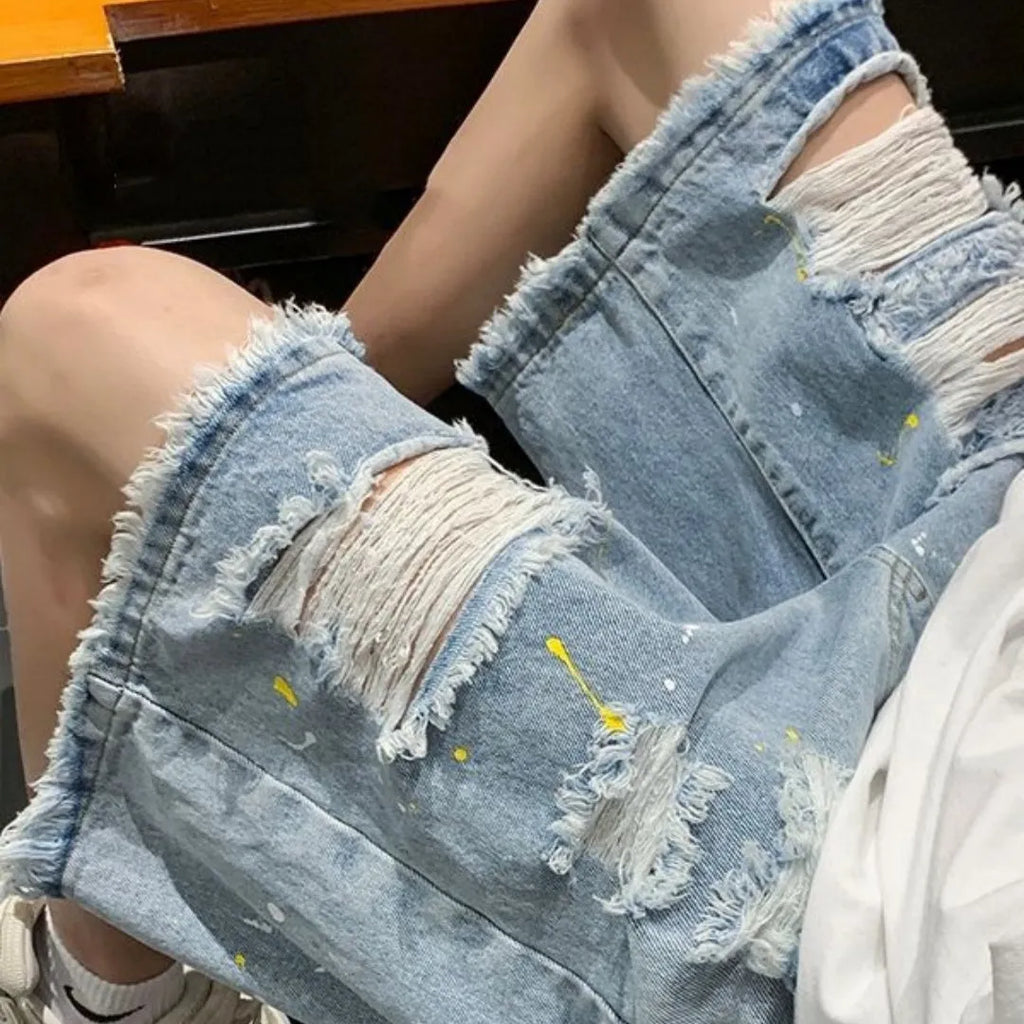 Man wearing loose-fit light blue denim shorts with a water-washed finish and distressed holes.