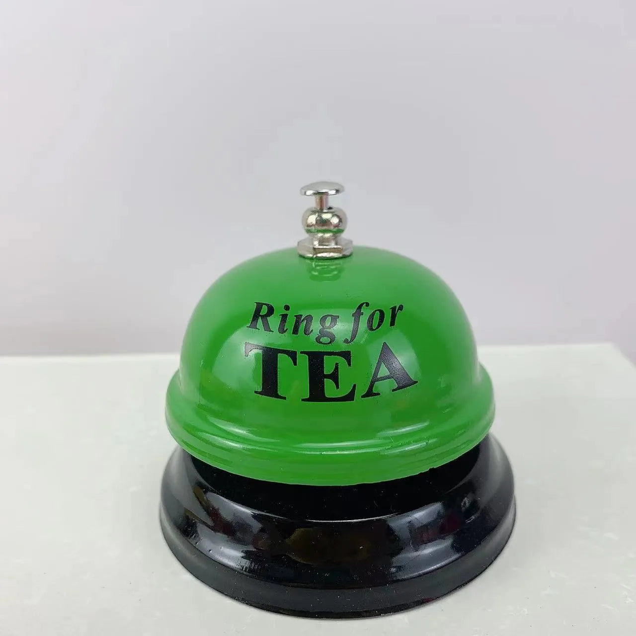 Iron call bell on a desk, shown in one of twelve available colours including red, blue, green, and pink.