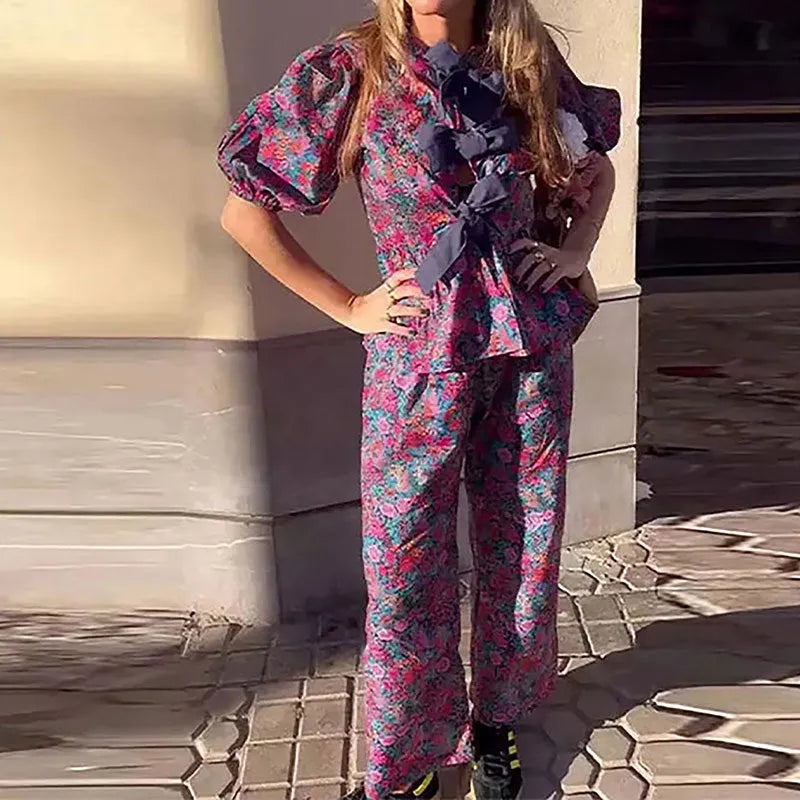 Women's floral print tie-neck blouse and trousers suit with puff sleeves.