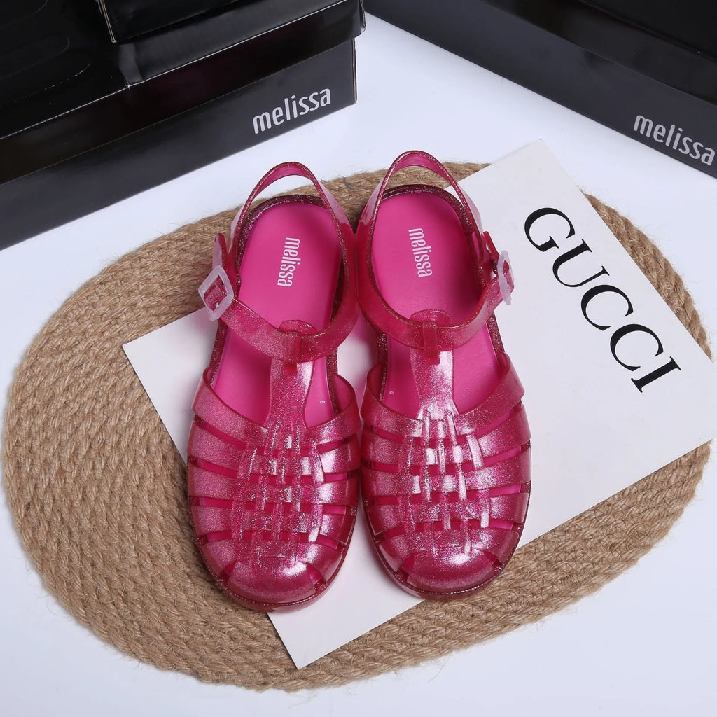 A pair of black PVC Roman sandals with a buckle fastening and hollow-out pattern on a white background.