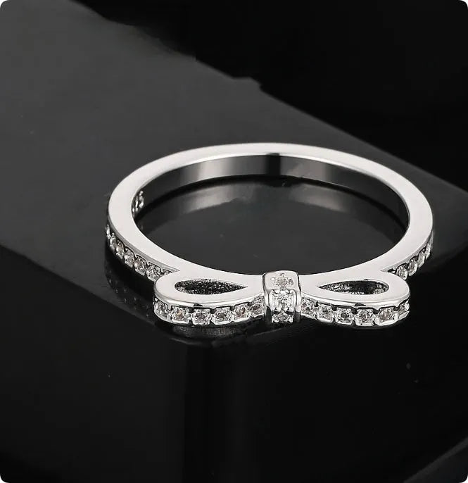 Silver bow-shaped ring with zircon crystals on a finger, showing detailed bow motif design