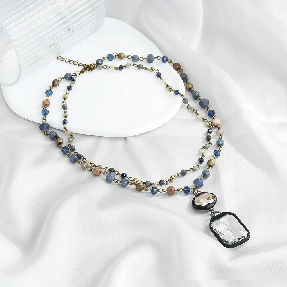 Tribal-style layered necklace with glass pendant and adjustable chain in beige or blue.