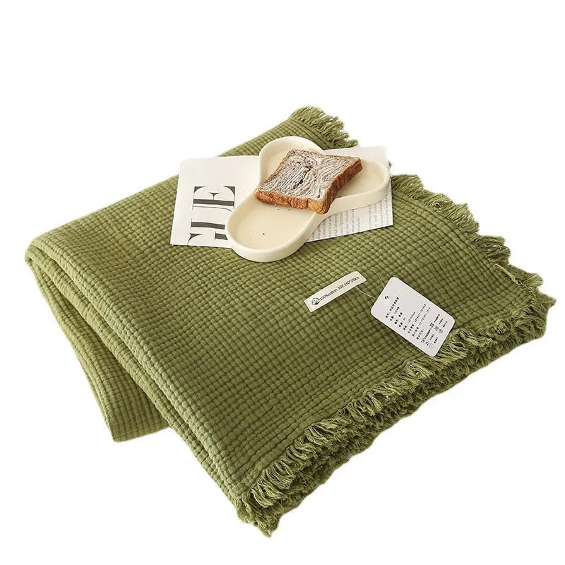 Four-layer cotton gauze blanket with tassel trim in avocado green colour laid flat.