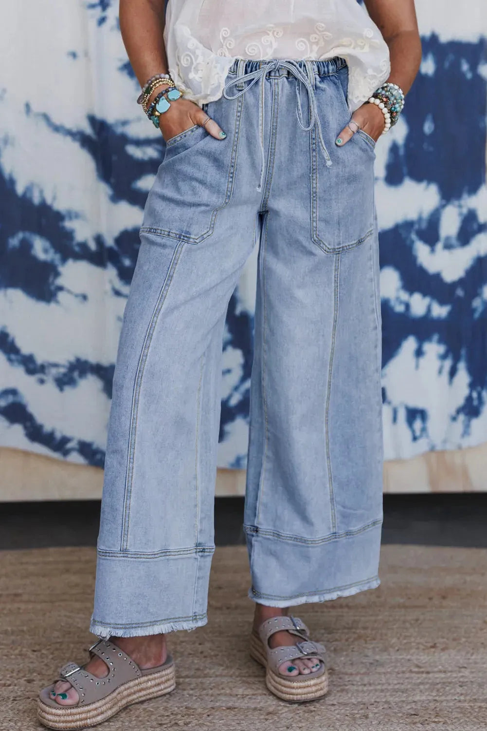 Beau blue wide leg denim pants on a hanger, showing drawstring waist and raw hem detail.