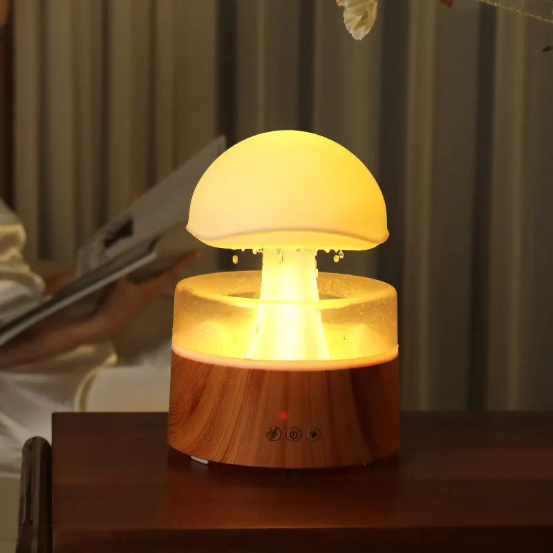 White cloud-shaped humidifier on a table emitting mist and showing coloured LED lights inside, with a remote control beside it.
