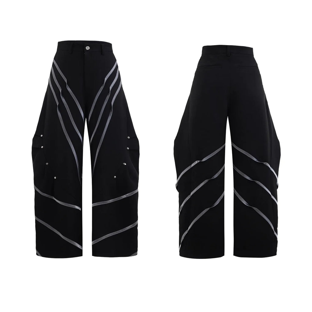 Men's black trousers with metal rivet pleats and a tapered leg, showing three-dimensional cutting.
