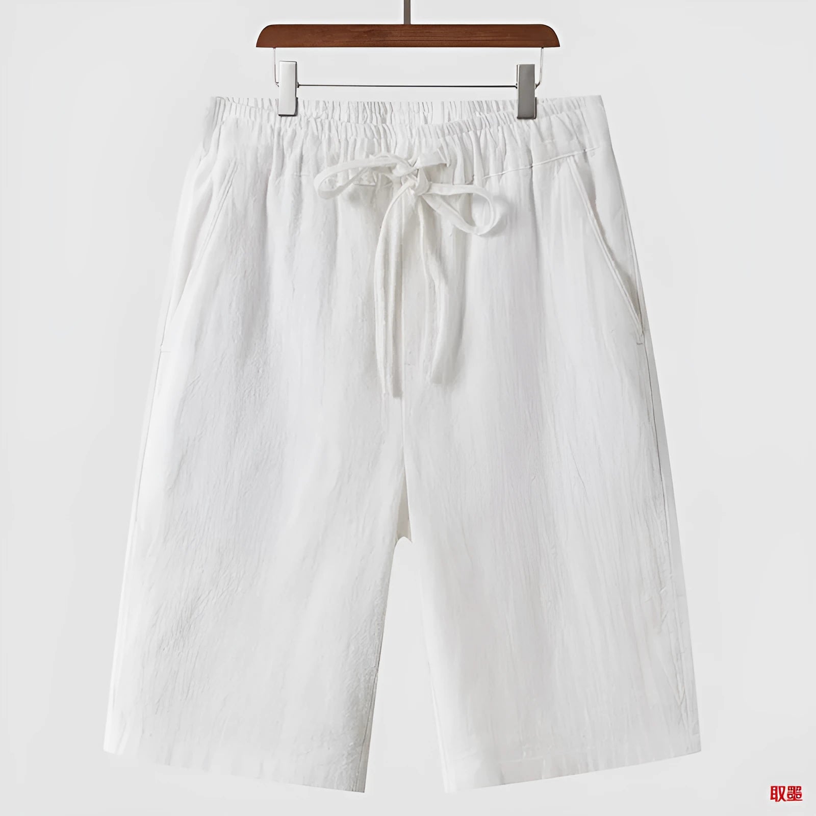 Men's beige linen casual shorts with loose cropped fit and elastic waistband on a neutral background.