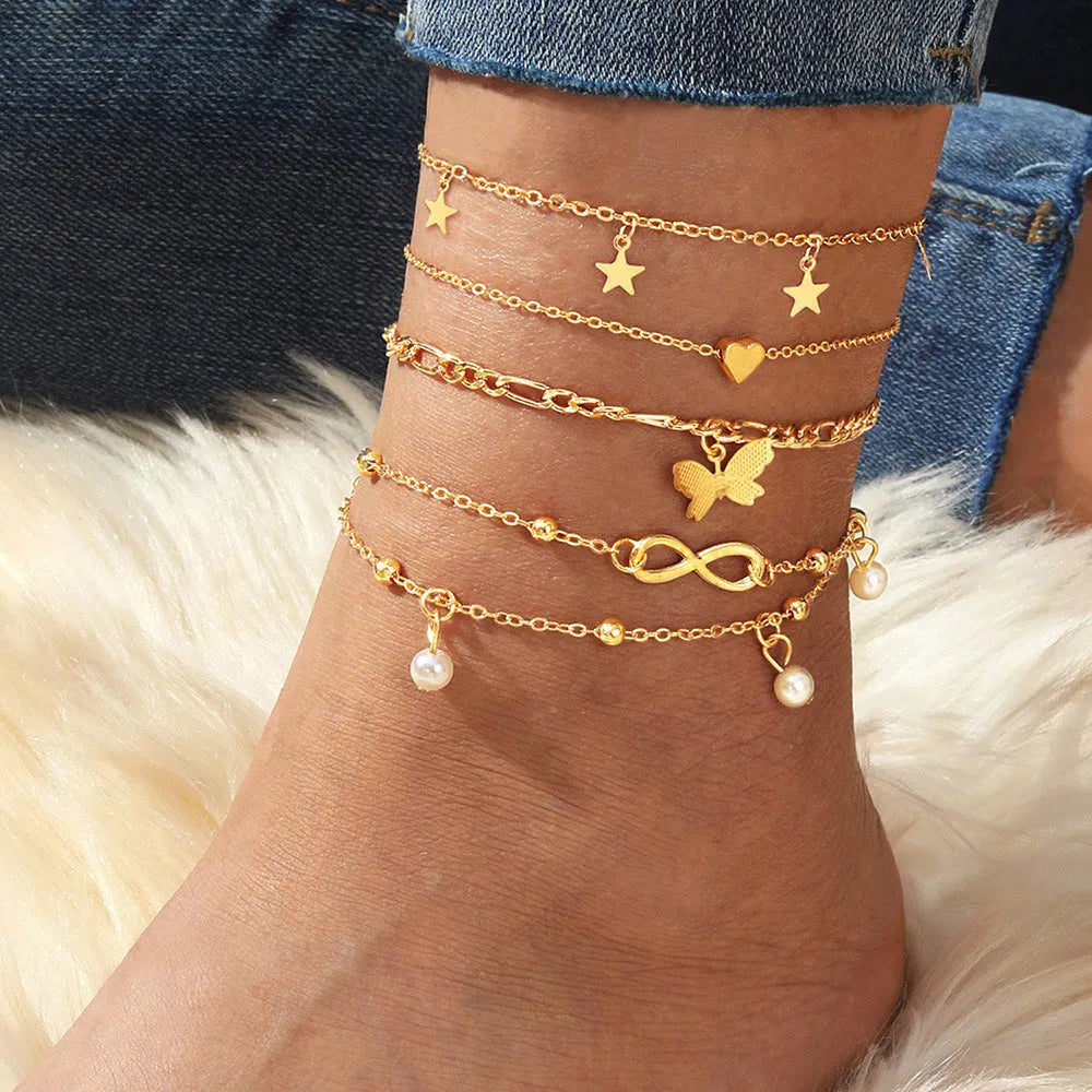Four different alloy anklets with butterfly and pearl heart pendants arranged as a jewellery set