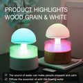 White cloud-shaped humidifier on a table emitting mist and showing coloured LED lights inside, with a remote control beside it.