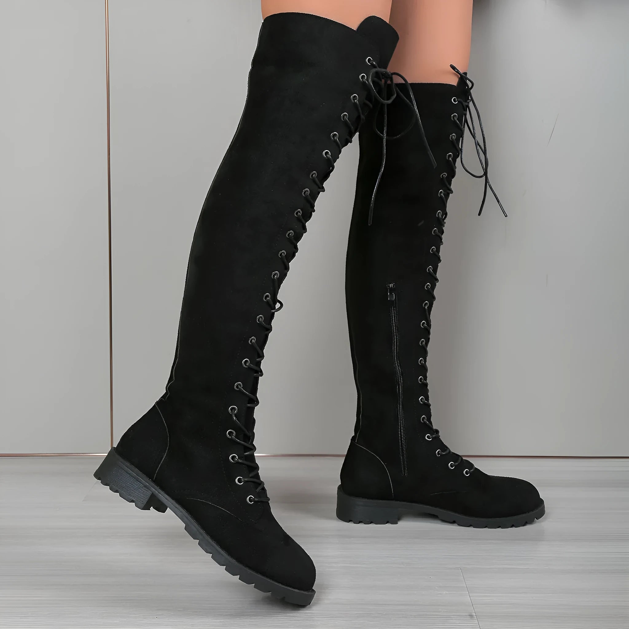 A pair of black lace-up over-the-knee boots with a round toe and flat rubber sole on a white background.