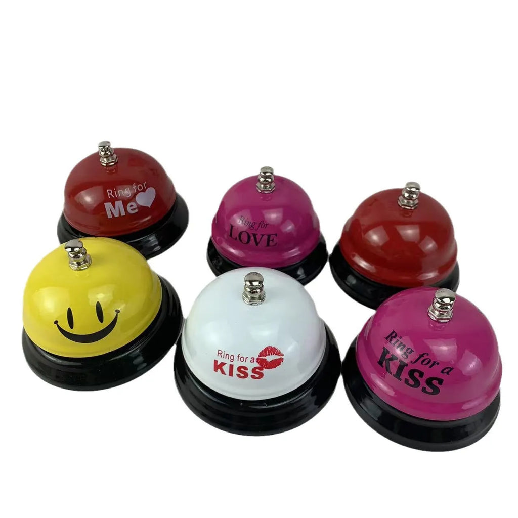 Iron call bell on a desk, shown in one of twelve available colours including red, blue, green, and pink.