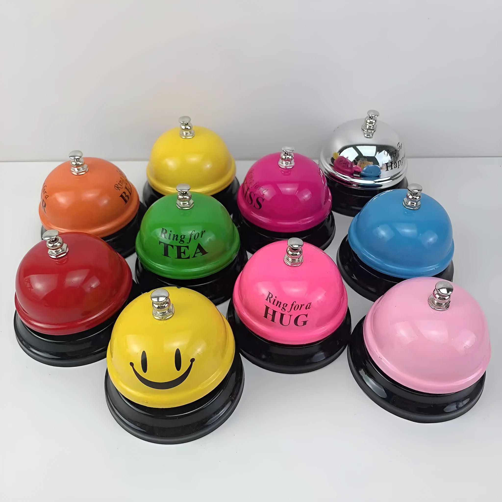 Iron call bell on a desk, shown in one of twelve available colours including red, blue, green, and pink.