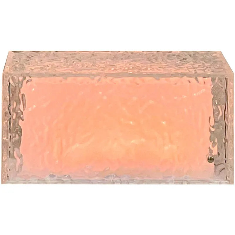 Clear acrylic ice cube shaped night lamp with coloured LED light on a table.