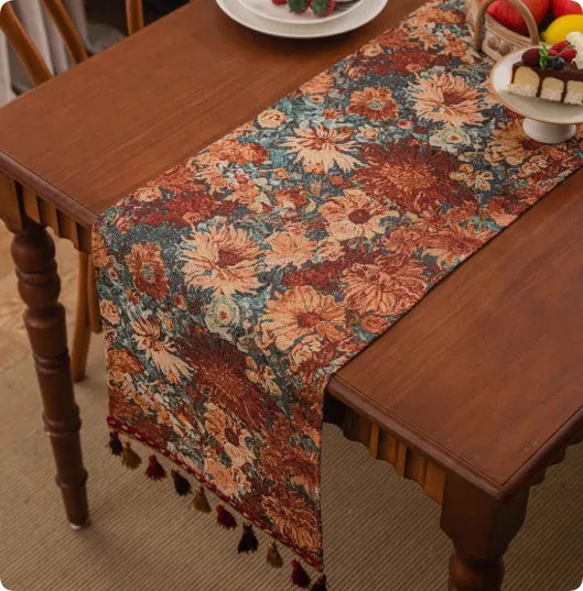 Long decorative table runner with handwoven tassels in a blue ginkgo leaf pattern on a wooden table.