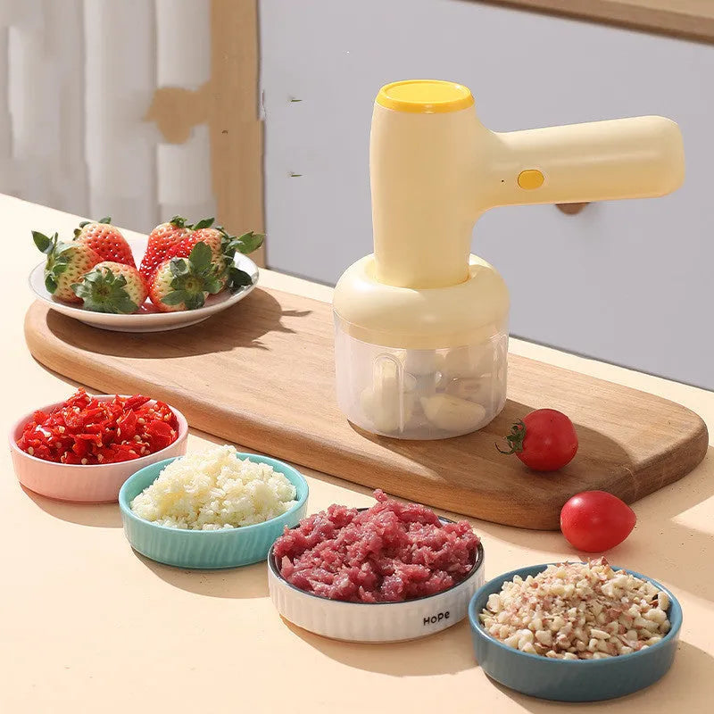 Beige electric garlic chopper with USB charging cable, 250ml cup, and stainless steel blade on kitchen counter