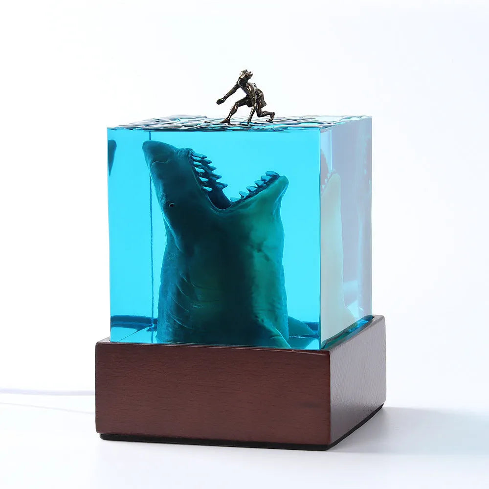 Clear epoxy resin ornament with a detailed shark surfing scene inside, shown next to its integrated lamp holder.