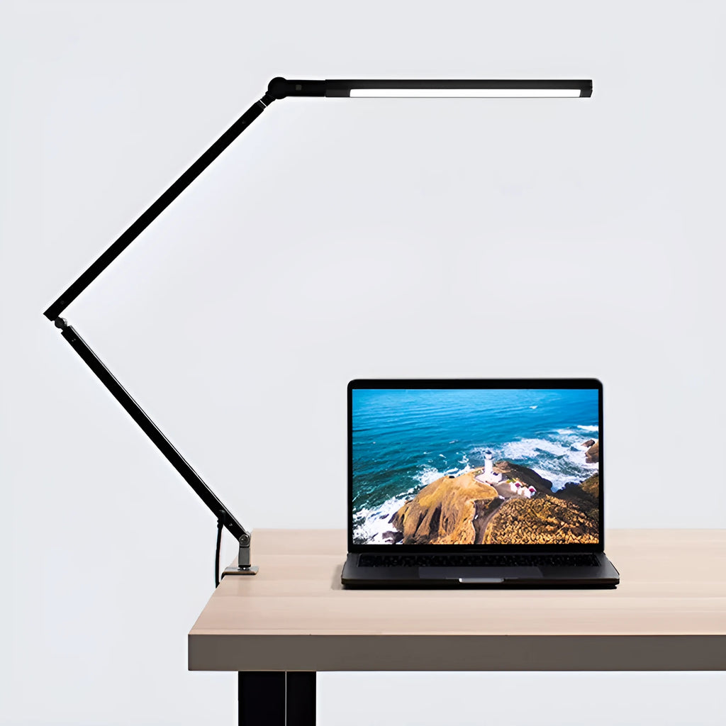 A black foldable LED desk lamp with a metal clip attached to a wooden desk edge, remote control nearby.